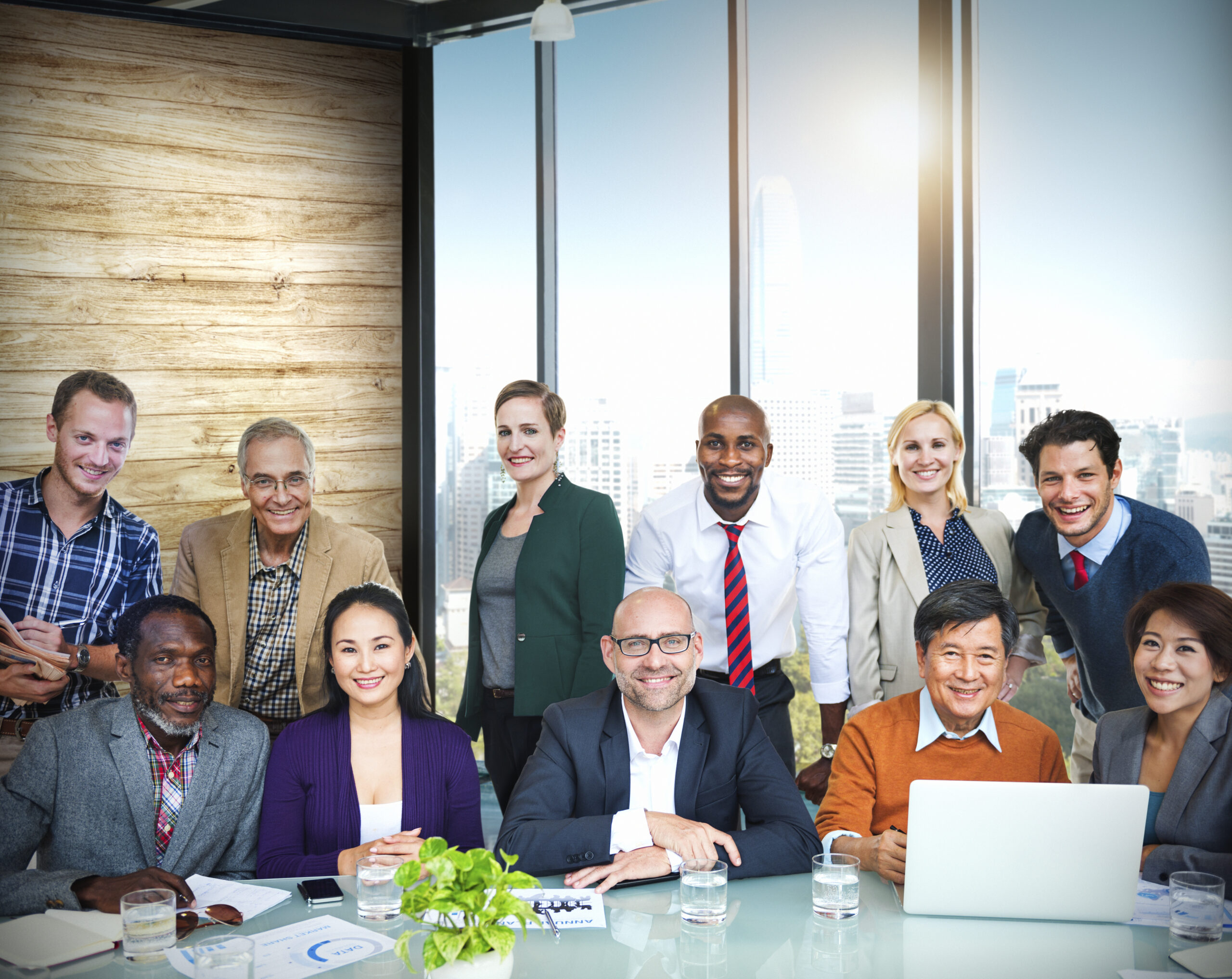 A team of diverse employees sitting and standing around a table in a conference room and smiling at the camera.