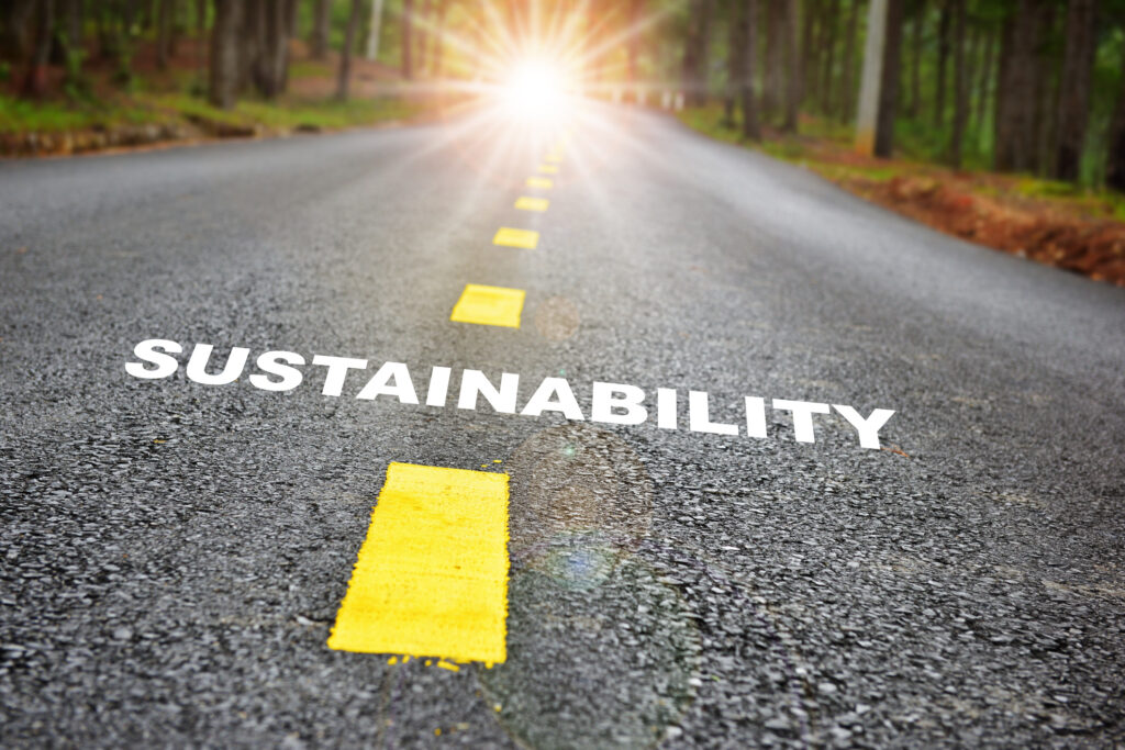Road with yellow dotted line divider and the word sustainability painted on the ground.