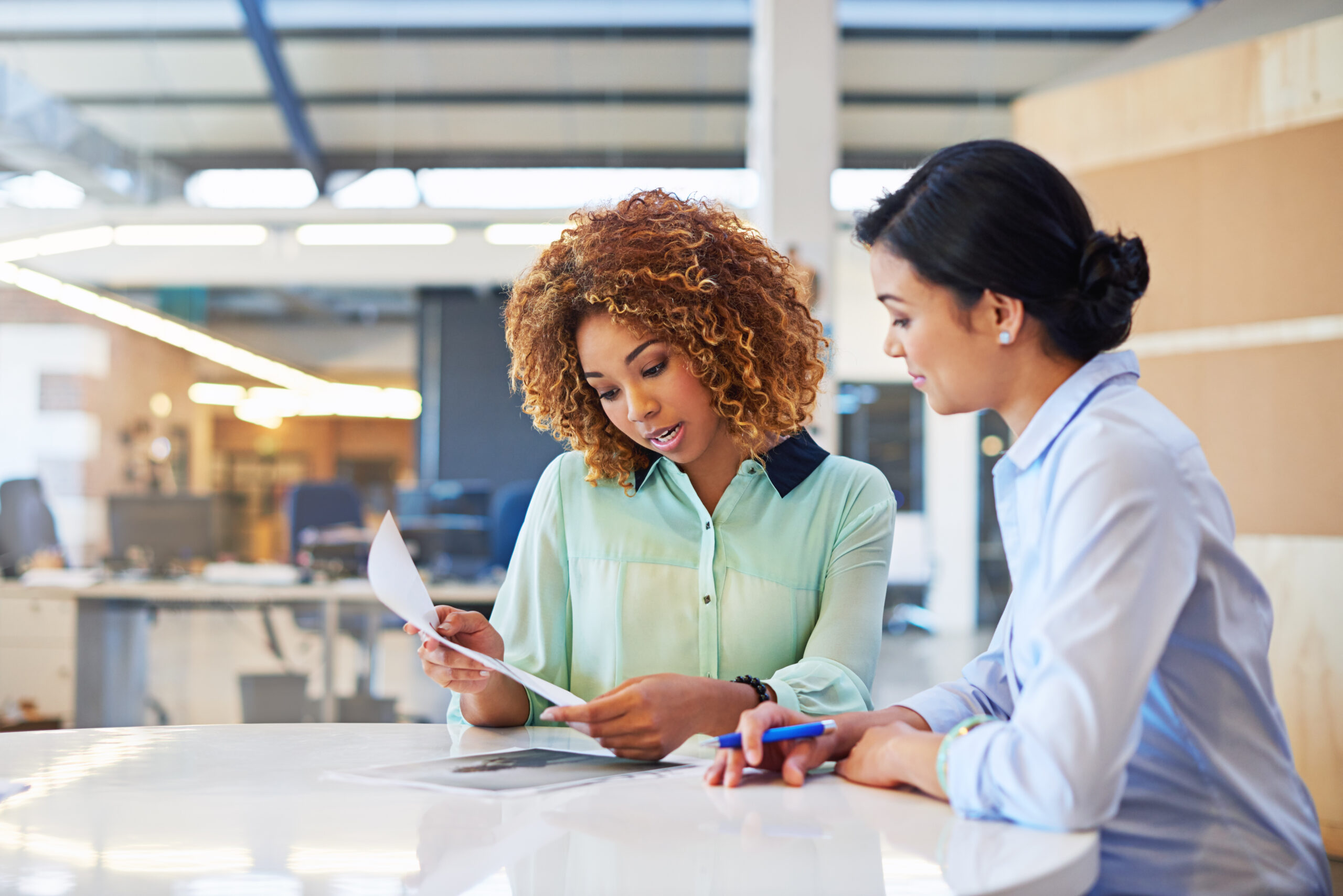 Women meeting at a table in an office looking at a paper together.