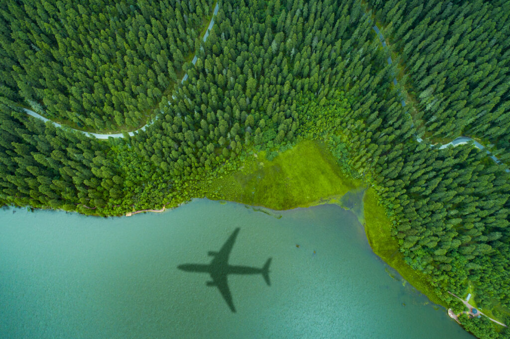 View down from the sky of the reflection of a plane over a lake and forests with a road between.